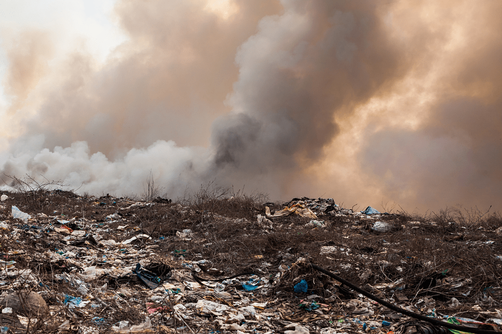 Large landfill with waste piles and methane collection infrastructure under a cloudy sky.